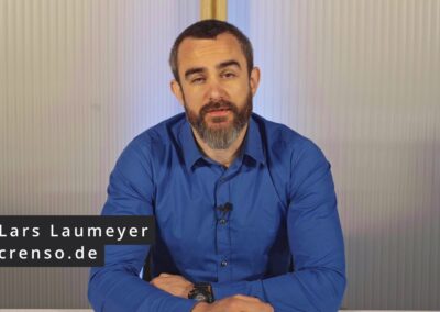 Das Bild zeigt Lars Laumeyer, der in einem Innenraum vor einer strukturierten, hellen Wand sitzt. Er trägt ein blaues Hemd und hat dunkles Haar sowie einen dichten Vollbart mit grauen Anteilen. Vor sich auf dem Tisch hat er die Arme verschränkt, an seinem Handgelenk trägt er eine schwarze Armbanduhr. An seinem Hemd ist ein kleines Mikrofon befestigt, was auf eine Videoaufnahme oder einen Vortrag hindeutet. Links unten im Bild ist ein schwarzes Textfeld eingeblendet mit der Aufschrift: „Lars Laumeyer crenso.de“ – dies gibt sowohl seinen Namen als auch seine Website an. Das Bild wirkt professionell und stammt aus einem Video im Rahmen eines E-Learning-Formats oder Interviews.