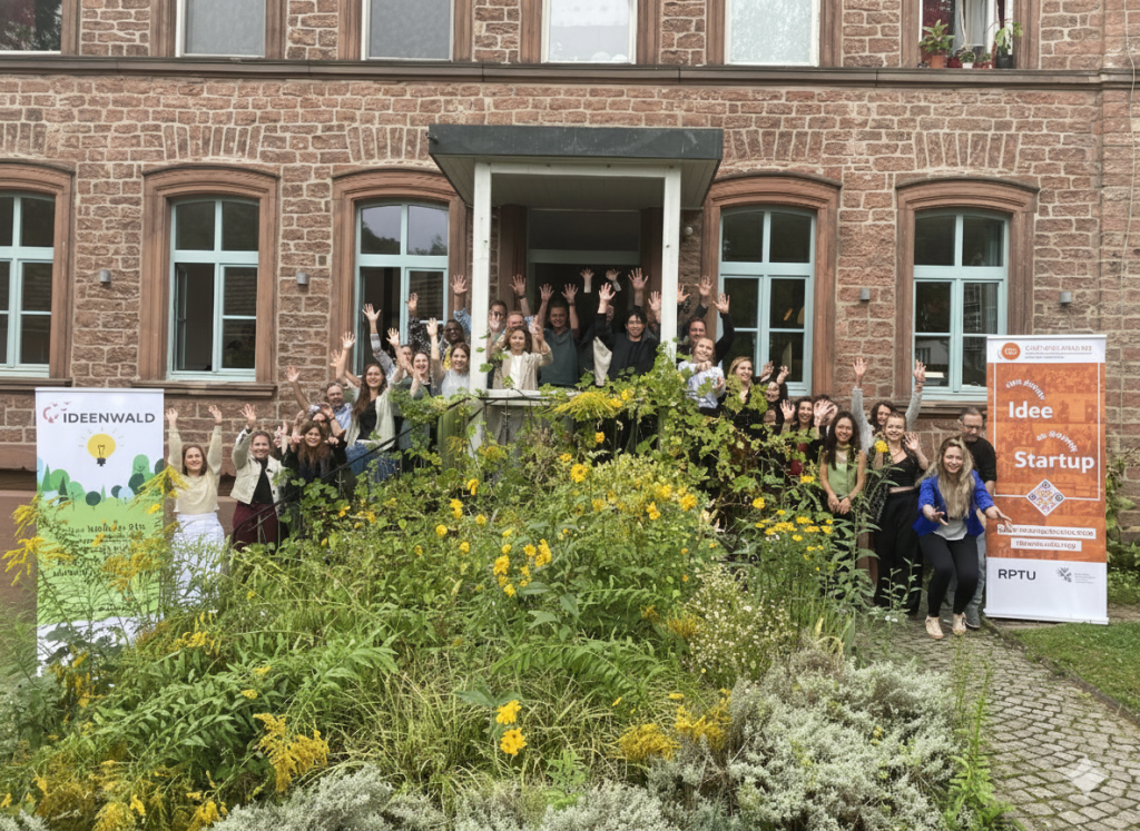 Gruppenfoto vor historischem Gebäude mit Bannern „Ideenwald“ und „Idee trifft Startup“.